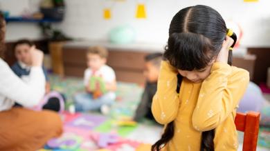 
		Ein autistisches Mädchen hält sich im Kindergarten die Ohren zu
	