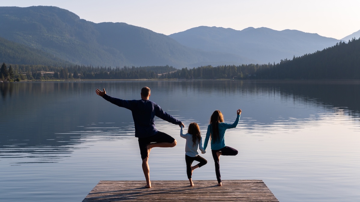 Vater steht mit seinen zwei Kindern auf einem Bein auf einem Steg am See