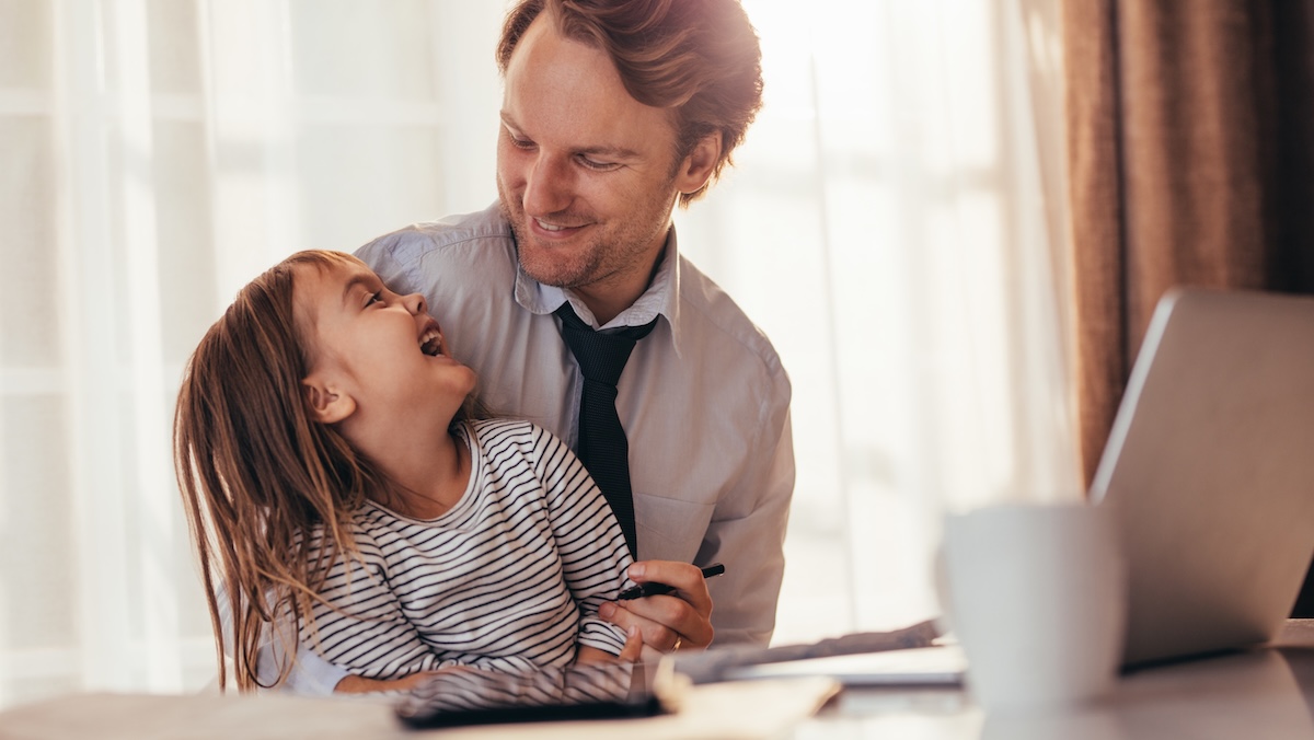 Vater sitzt vor Laptop mit Kind auf dem Schoss